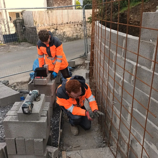 a picture of two workmen in high vis jackets building a wall