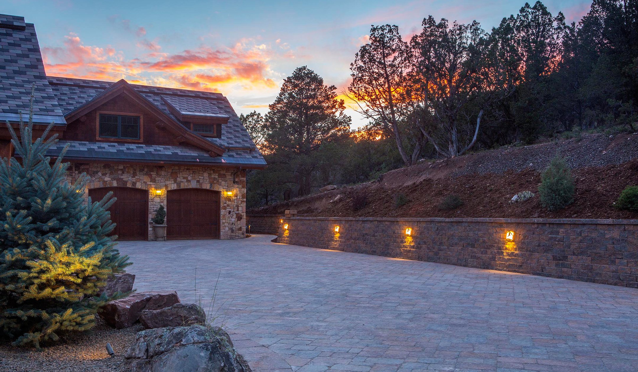 a driveway with stone walls and lights at sunset