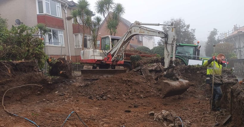 a digger is doing groundworks in front of a house